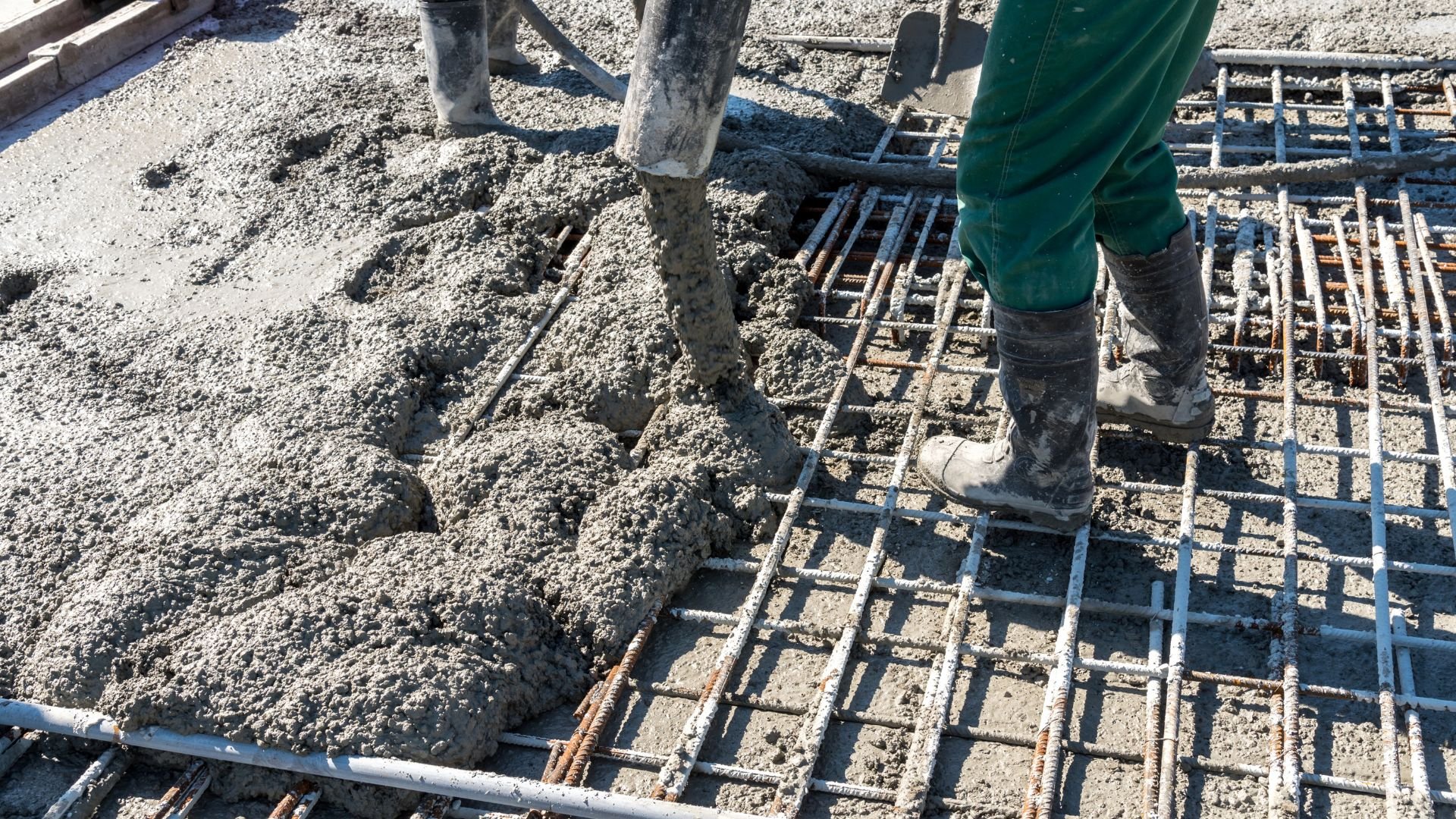 Construction worker pouring concrete over reinforced steel rebar grid
