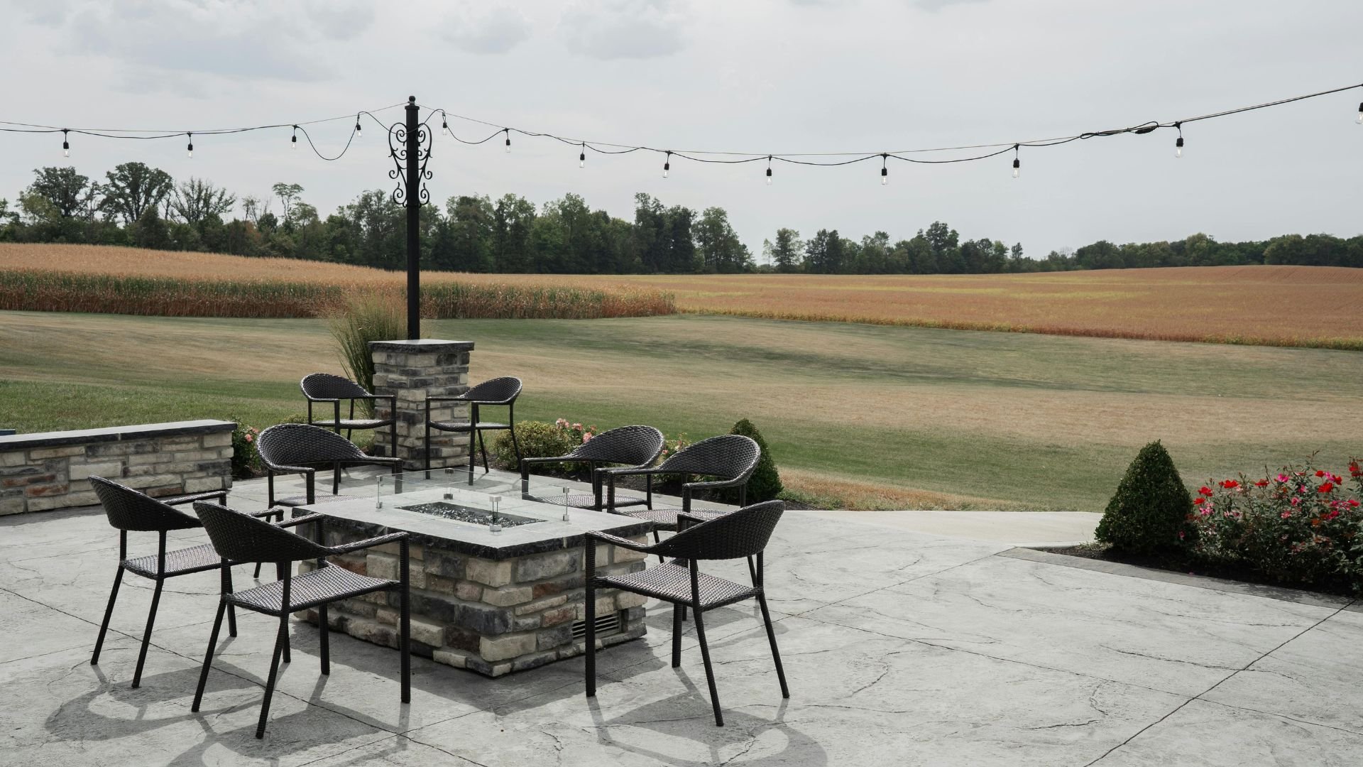 Outdoor patio with fire pit, chairs, and corn fields in background