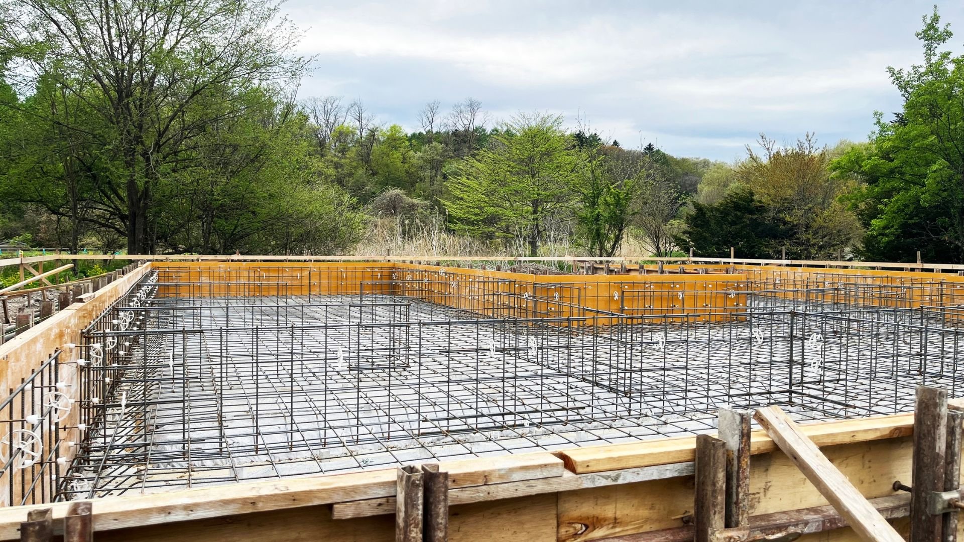Construction site with rebar and formwork, surrounded by green forest