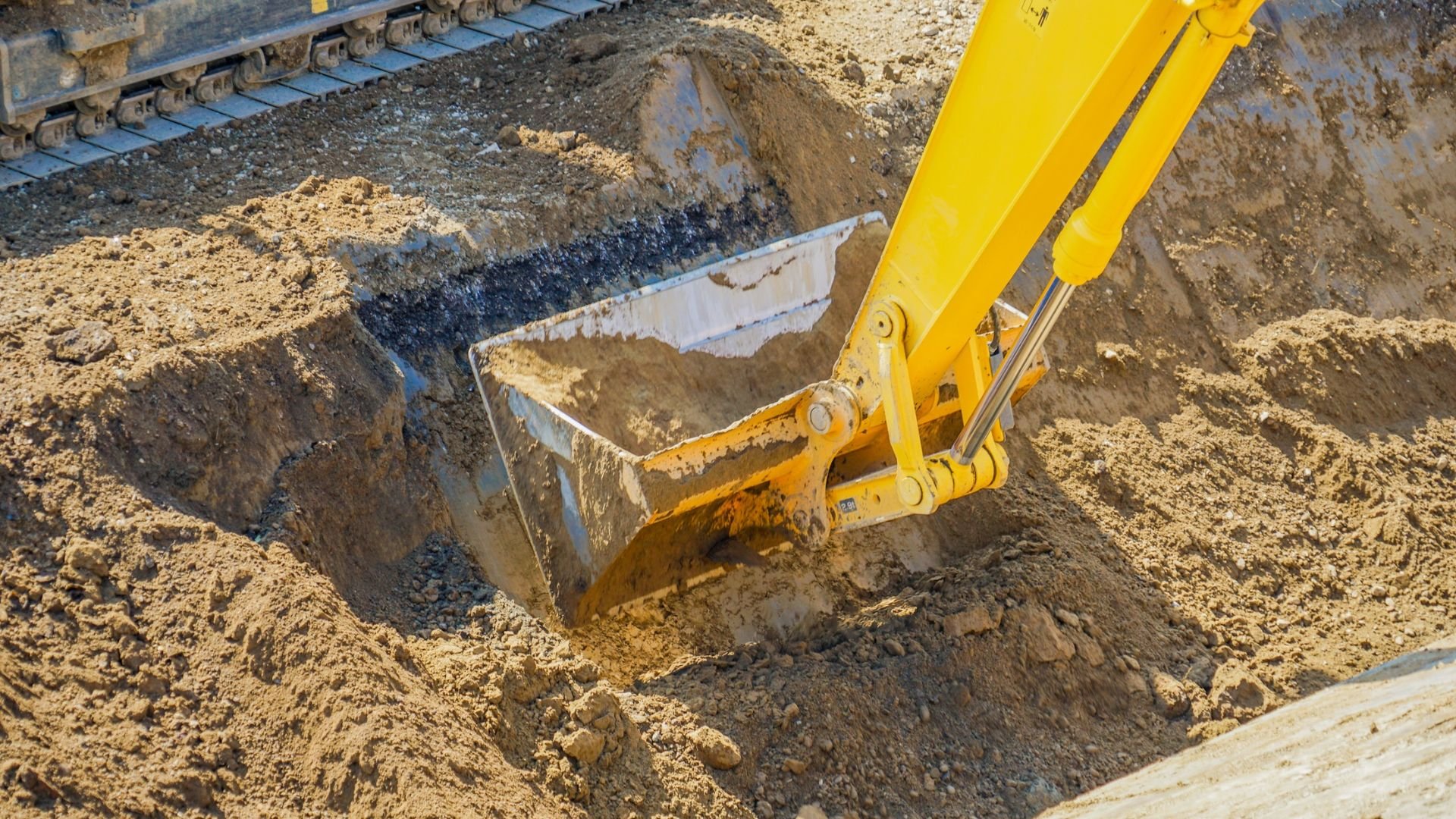 Yellow excavator digging deep hole in sandy construction site