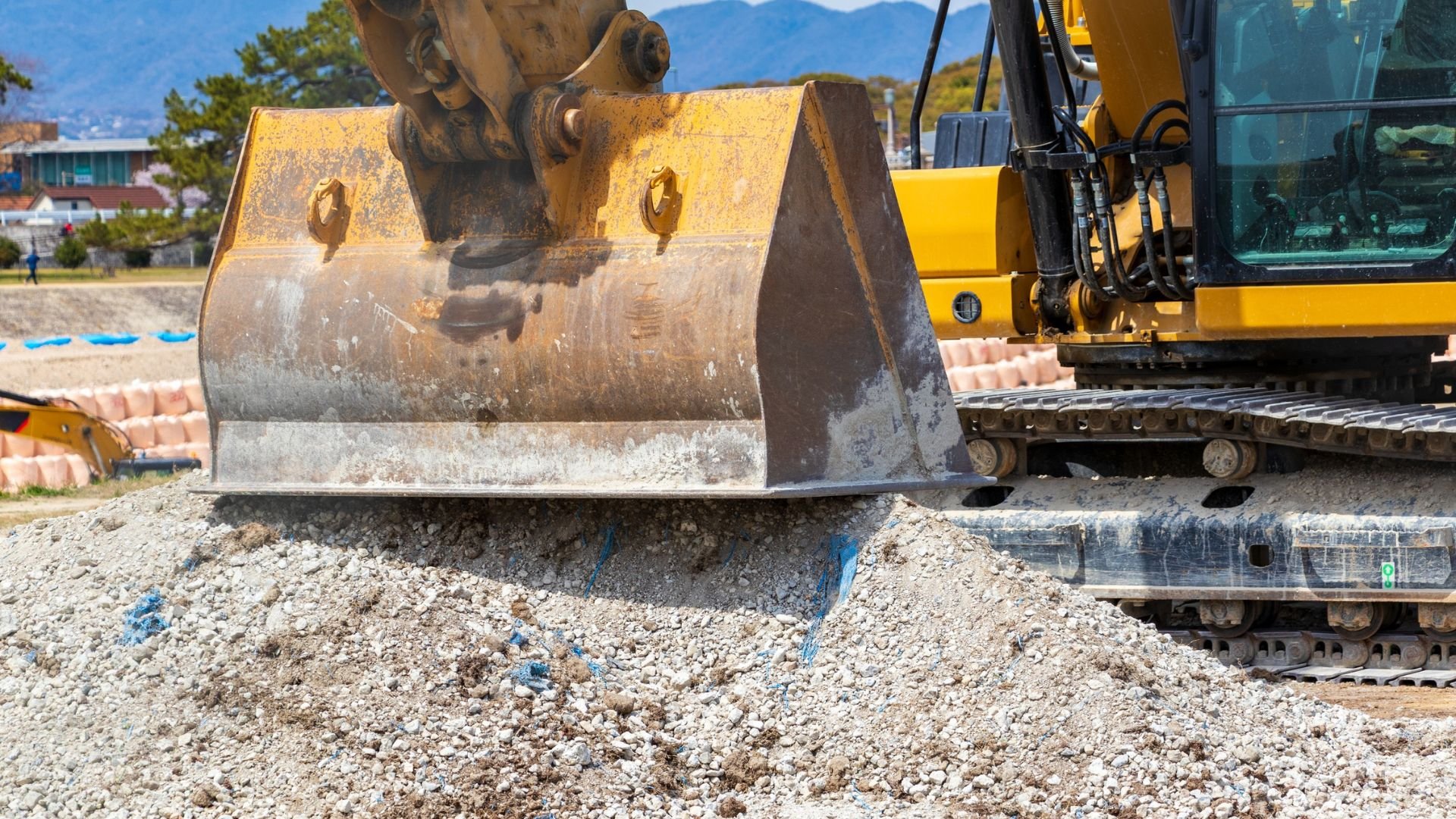 Yellow excavator with large bucket working on rocky construction site