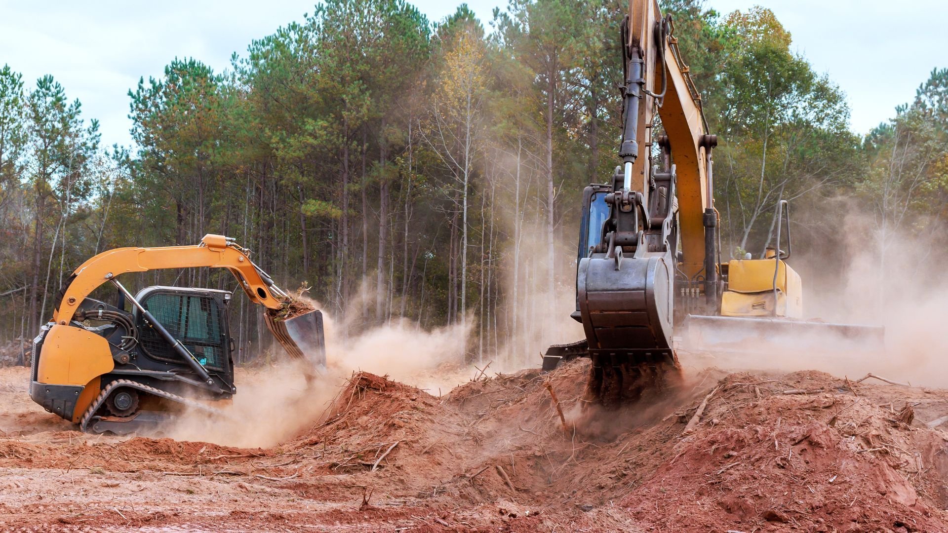 Two excavators clearing forest land, creating dust in woodland area