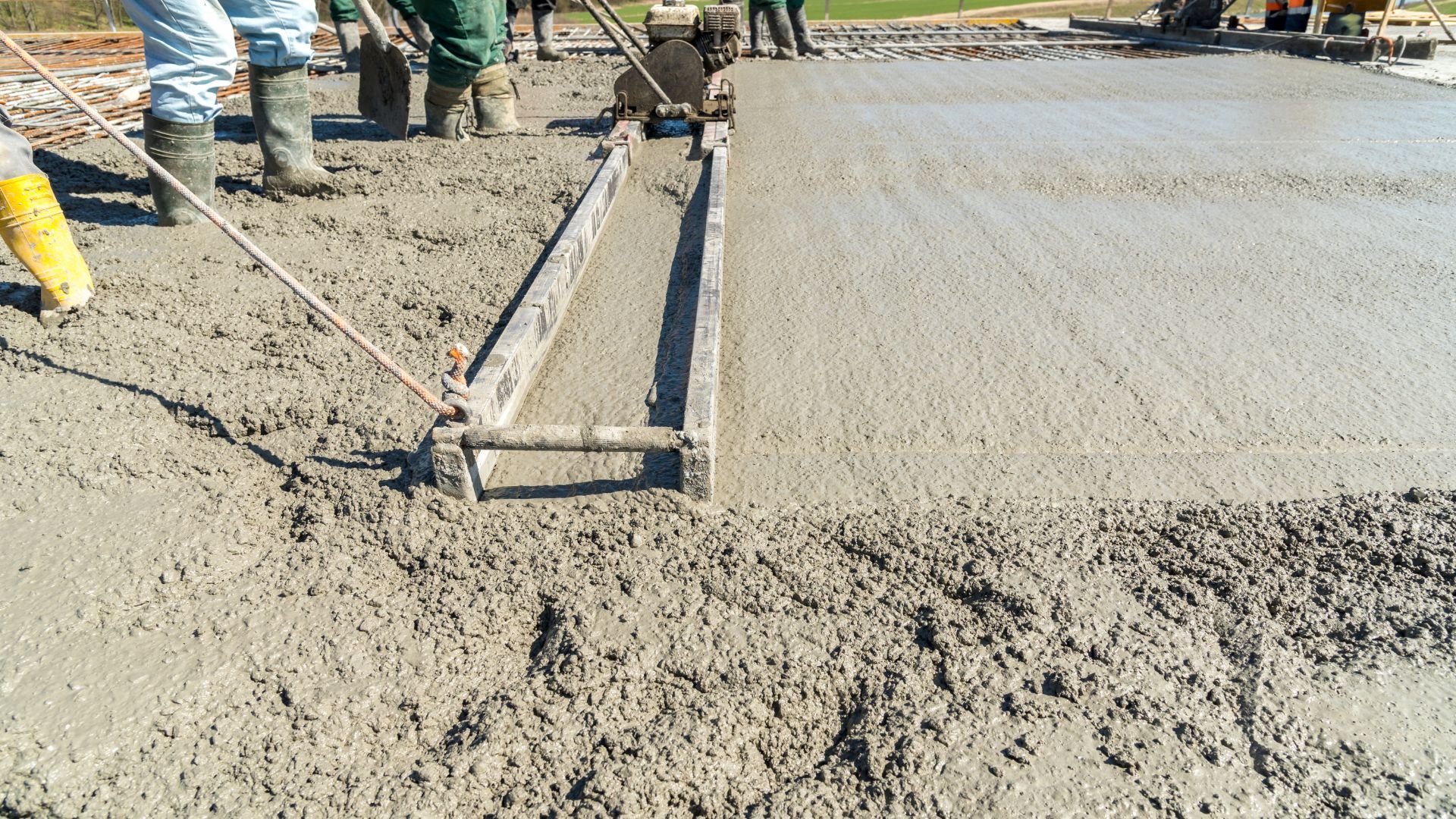 Workers smoothing wet concrete with leveling tool on construction site