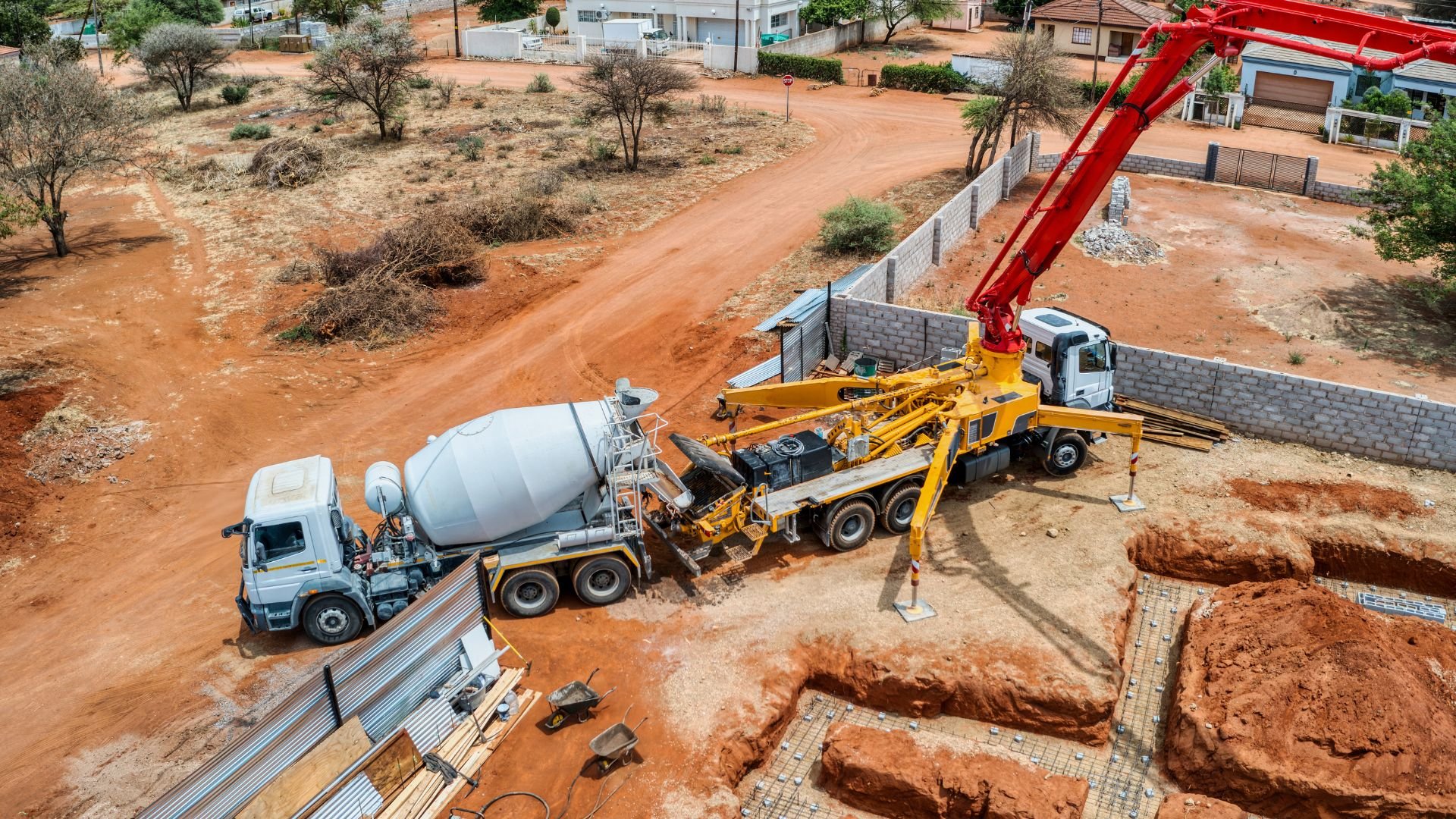 Construction site with concrete mixer and crane truck on red dirt road